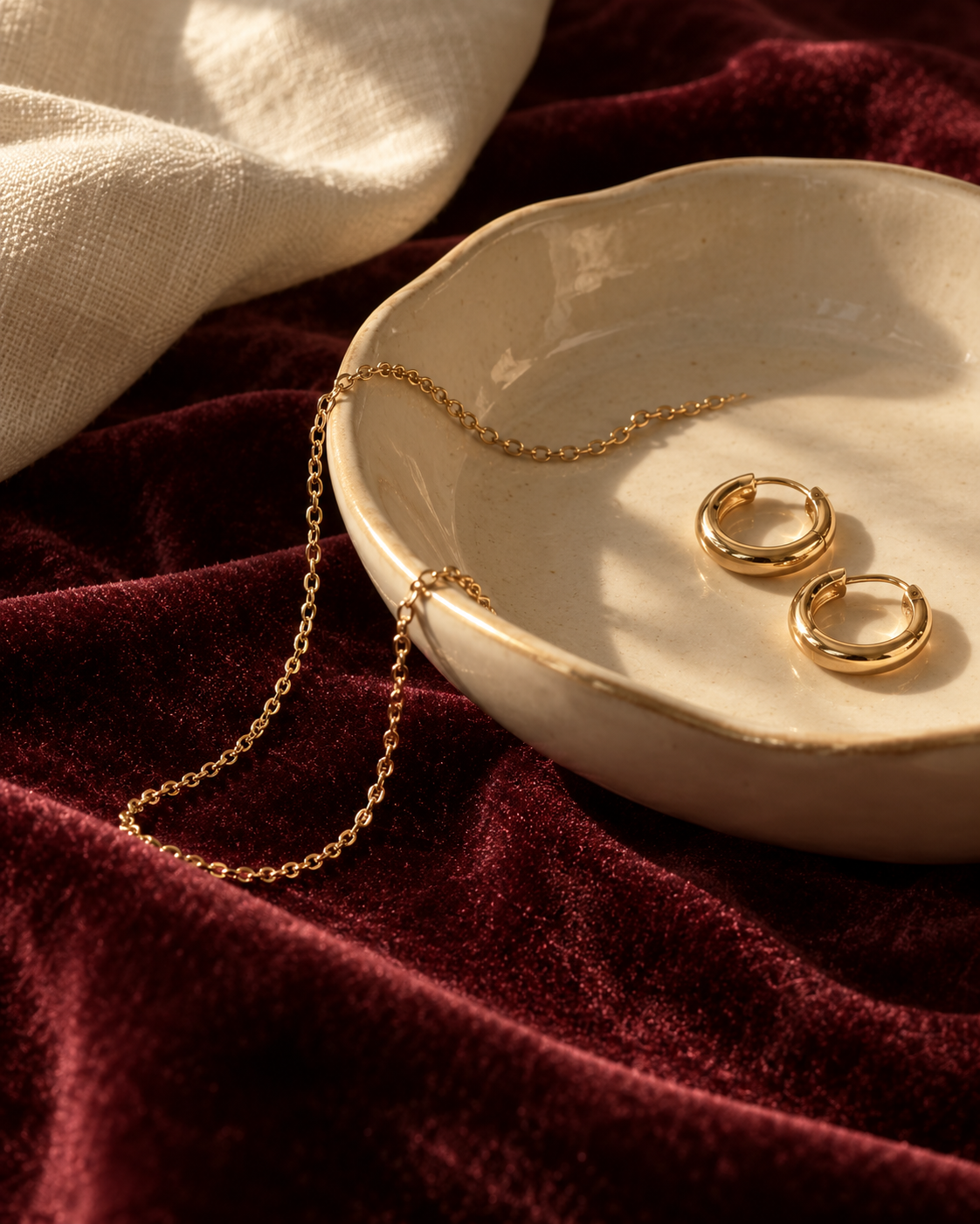Gold hoops and a delicate chain in an ivory dish on burgundy velvet